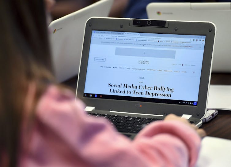 Si no aprendemos a los jóvenes sobre el ataque sexual y el consentimiento, los medios populares 2 El suéter rosa y la pantalla de la computadora en la que la pantalla tiene un artículo sobre ciberbuloso.