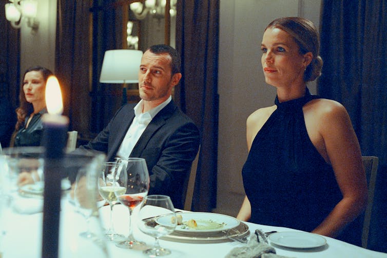 a woman in a black dress sits next to a man in dress shirt and jacket