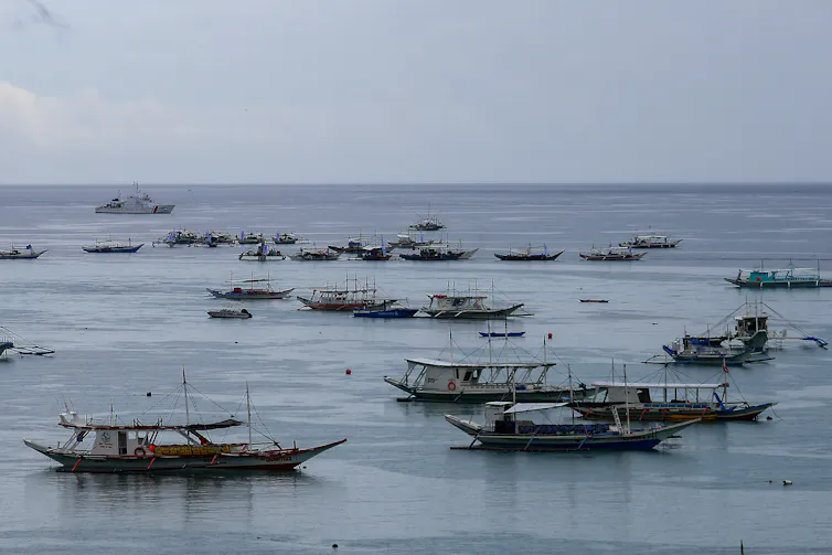 A dozen or so small ships are seen at sea.