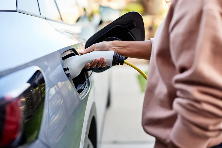 A person connects a plug to a car.