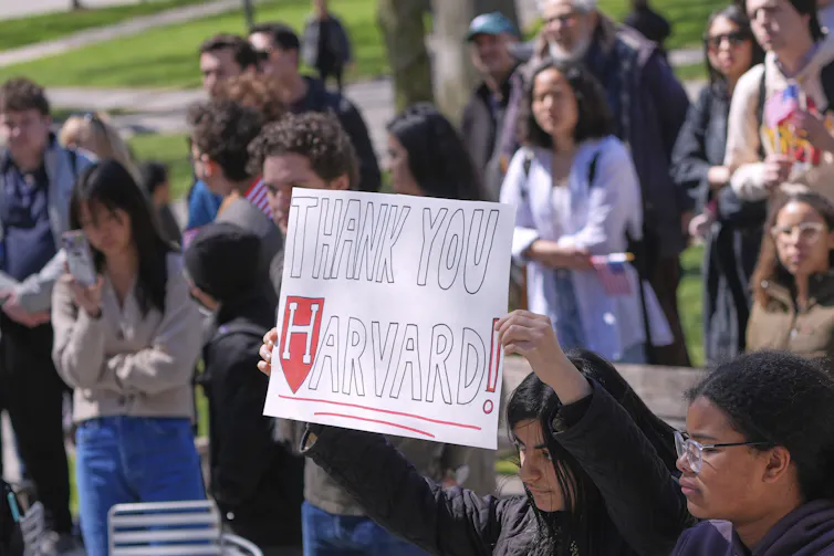 A person standing in a crowd of people holds up a sign that says 'thank you Harvard'