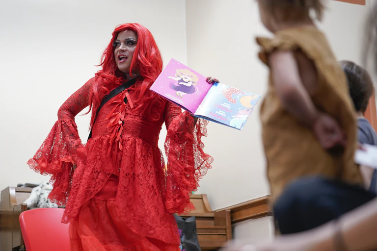 A person in lacy red dress and flaming red hair holds a book.