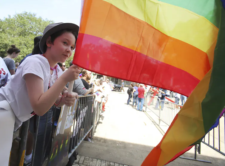 A young person waves a rainbow flag.