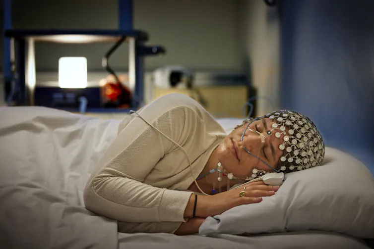 A woman lies in bed with an EEG cap.