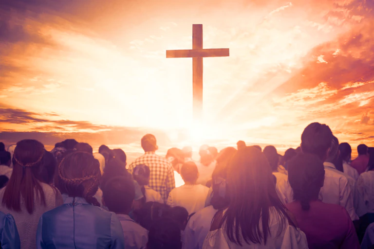 A crowd of people before a large cross surrounded by light.