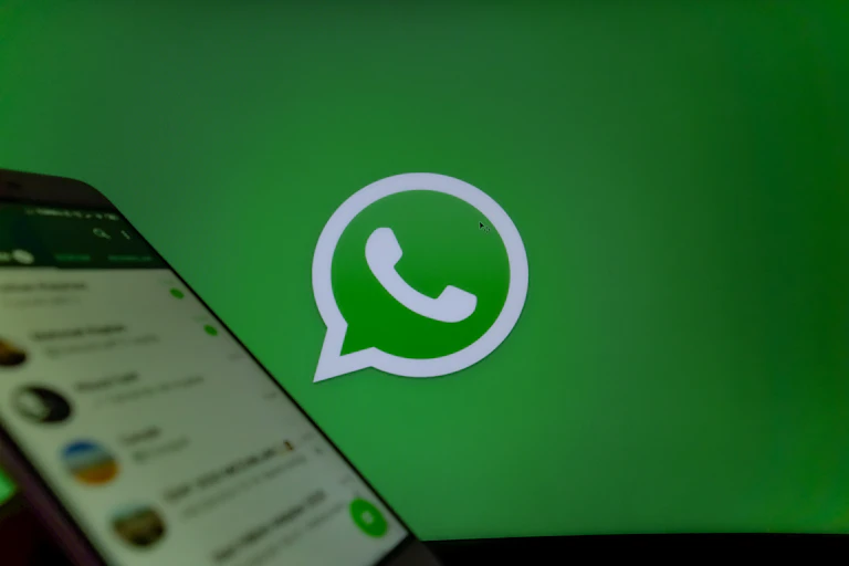 A green background with white whatsapp logo on it and a laptop screen in the foreground.