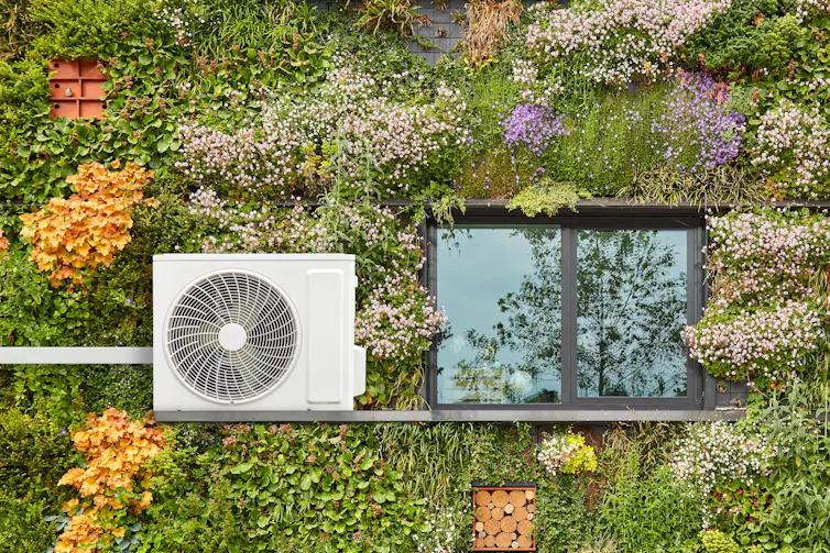An air-source heat pump on a house covered in plants.