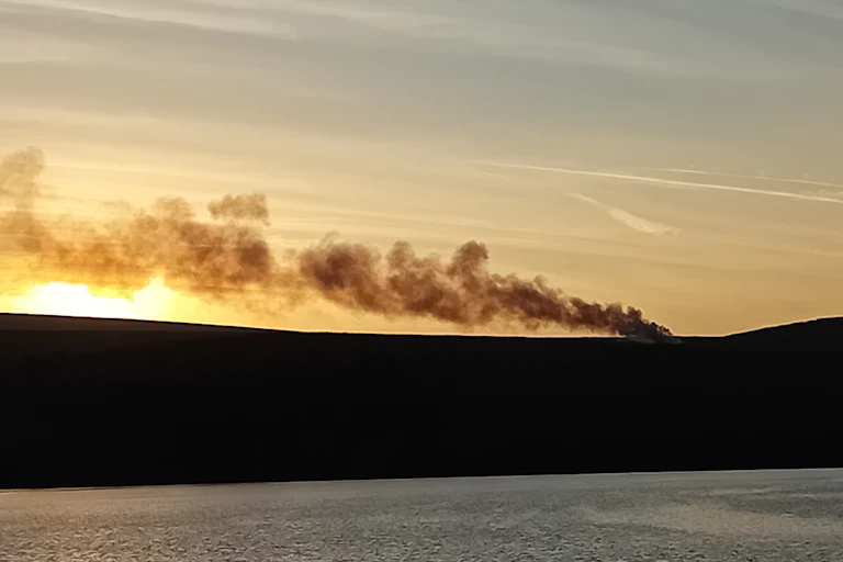 burning smoke from land, lake in foreground