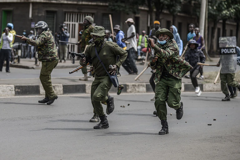 Armed police officers running on a road with a crowd of people behind them
