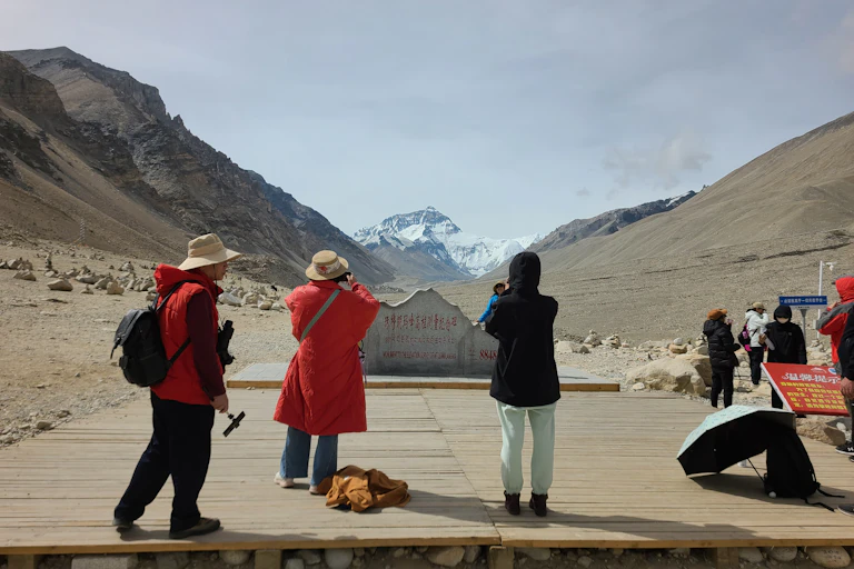 Turistas de costas para a câmera tiram fotos do Monte Everest à distância.