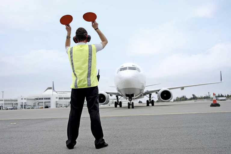 A person stands on an airport runway holding up circles to signal to an aircraft.