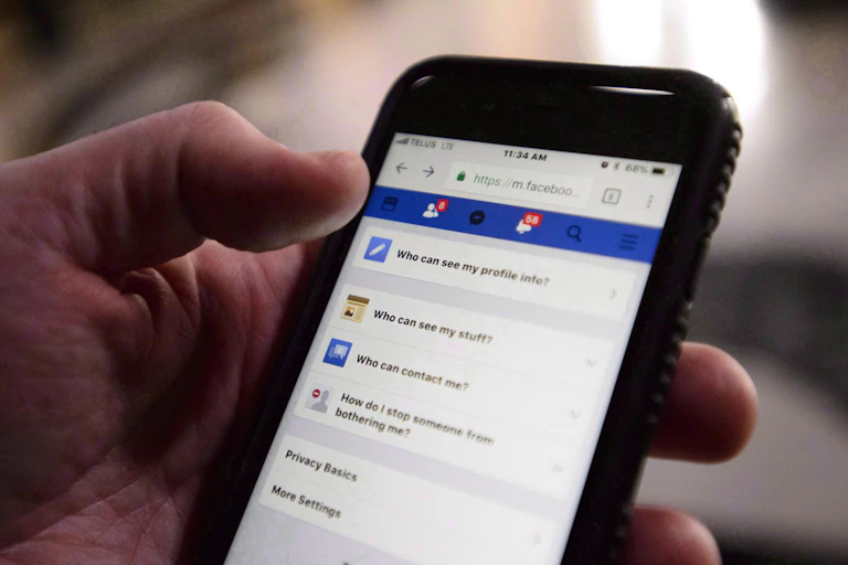 A person holds a smartphone open to Facebook privacy settings.