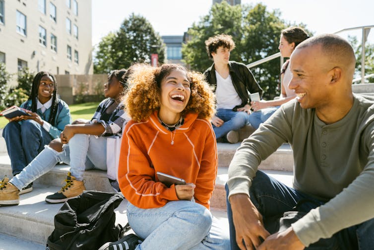 Students sit on steps talking to each other on a sunny day.