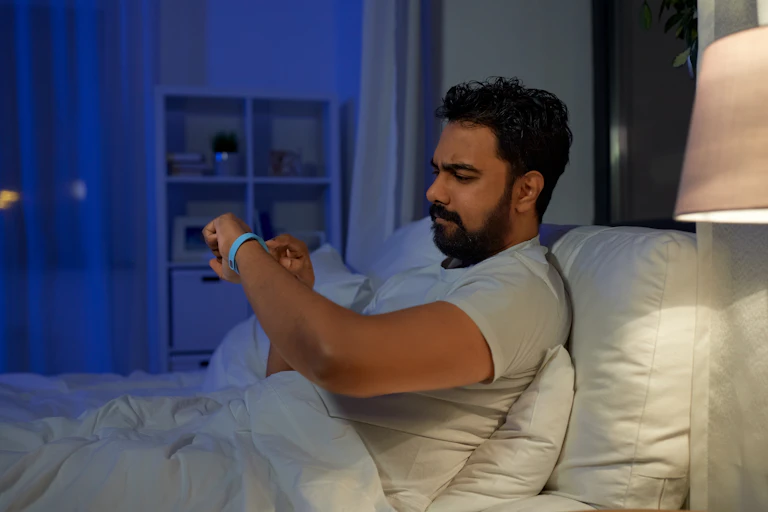 A man at night in bed checking his smart tracker on his wrist.