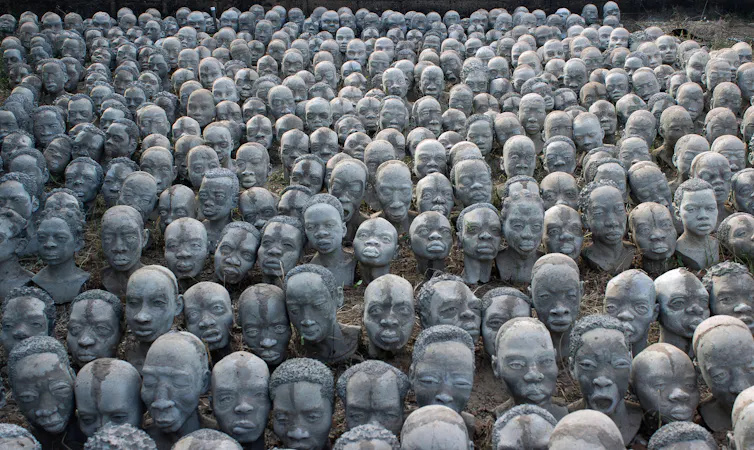 A sea of human heads coming from the ground, made in concrete.