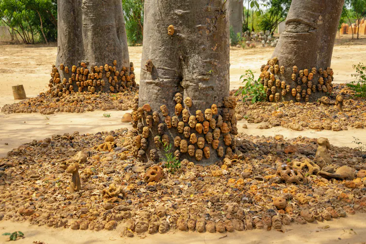 Trees, their bases lined with many small human heads in clay, broken heads forming large circles around the trees.