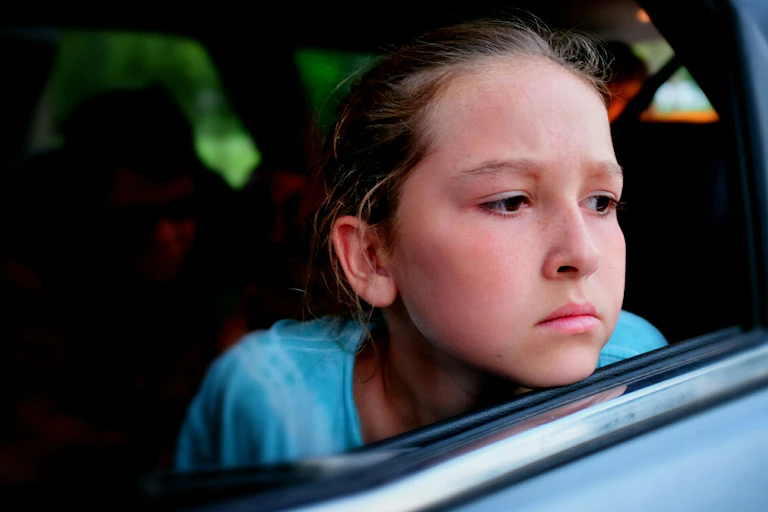 Nauseous-looking girl leaning out window of car.