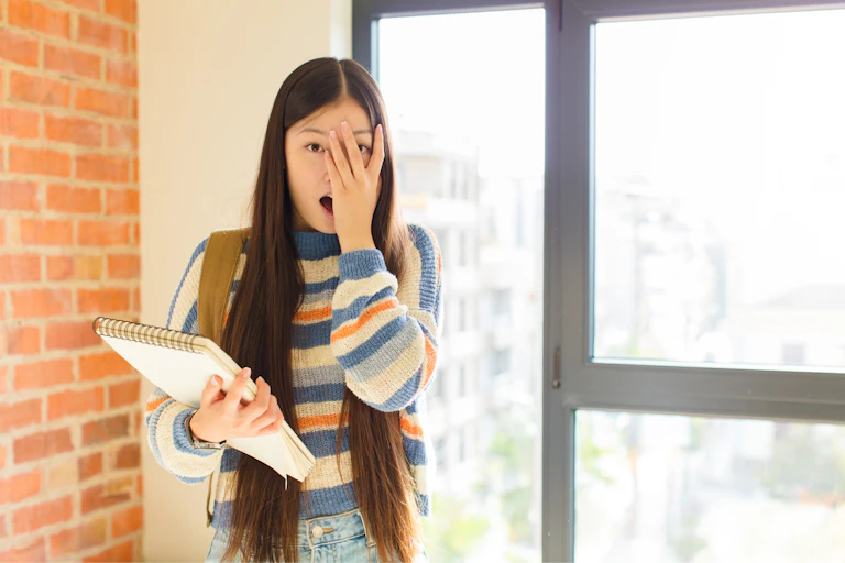 A young woman covers half of her face with her hand in embarrassment.