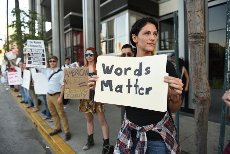 A dark haired female protestor, holding a sign saying 'Words Matter'.