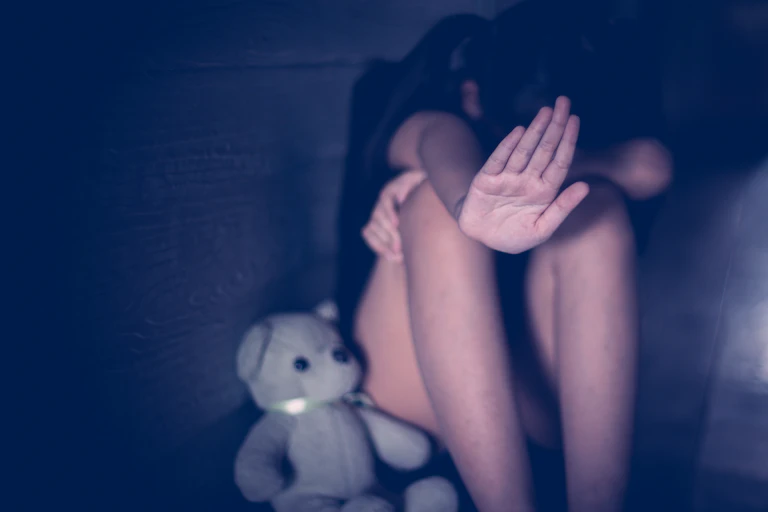 Una niña se tapa la cara y muestra la palma de la mano