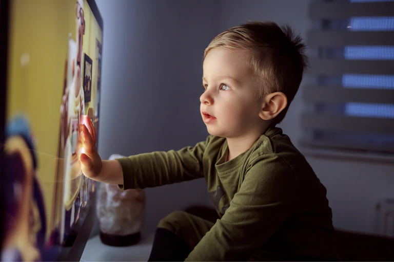 Un niño pequeño toca la pantalla de una televisión encendida