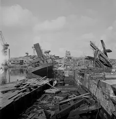 A black-and-white photo shows destroyed ships in a harbour.