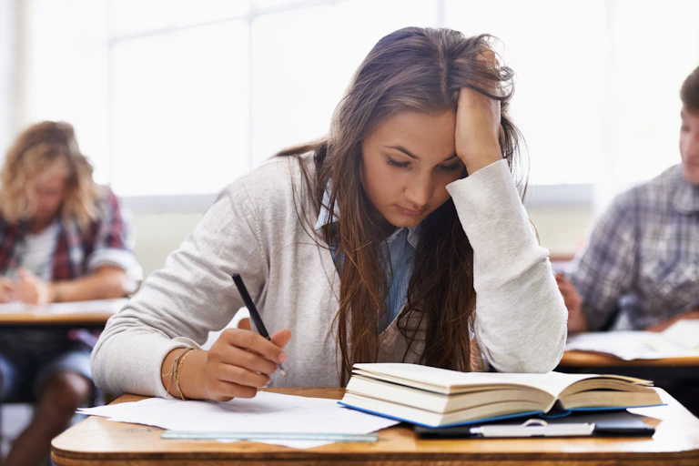 Una estudiante toma notas en clase con gesto de estar abrumada