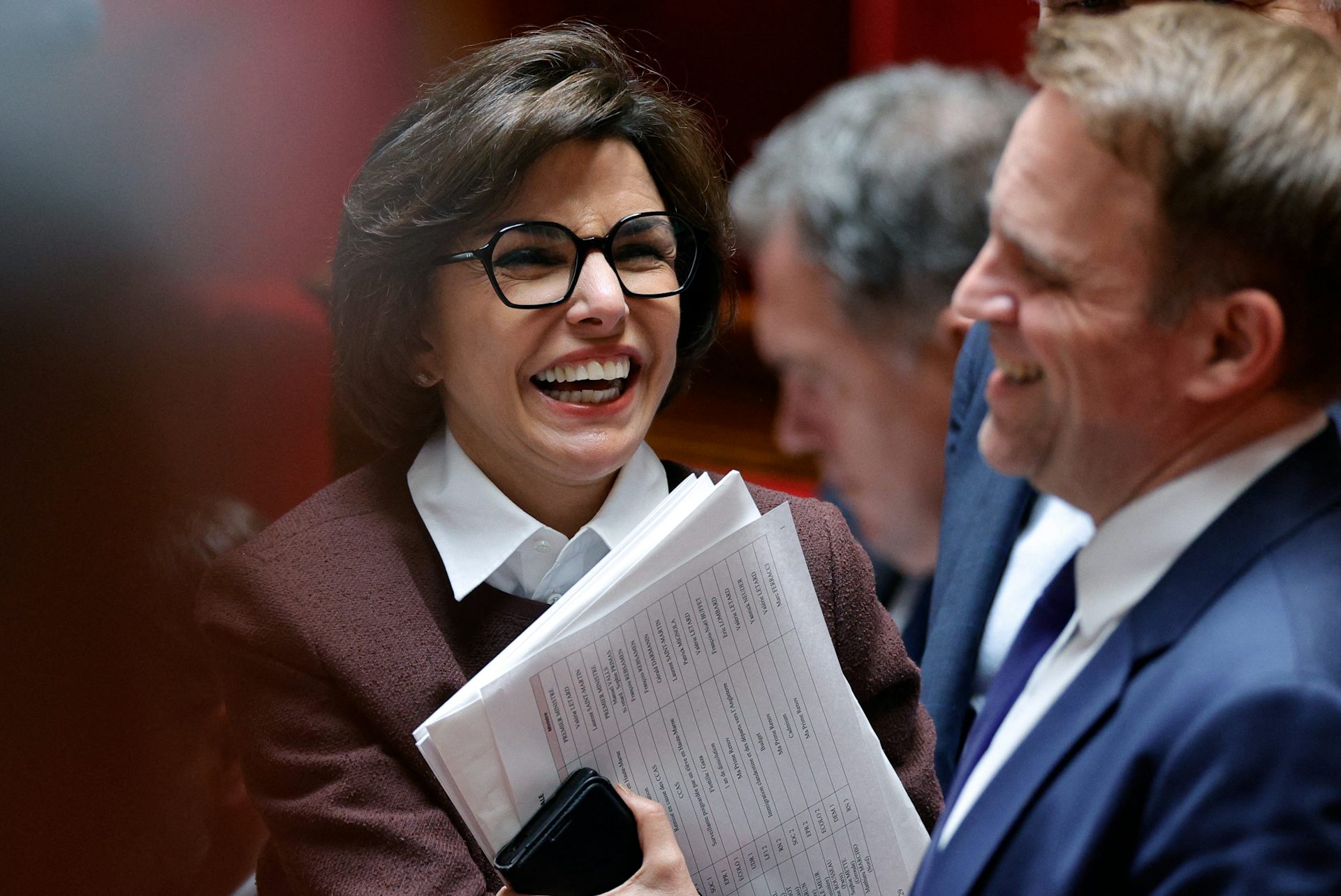 Une femme sourit devant les bancs de l'Assemblée nationale