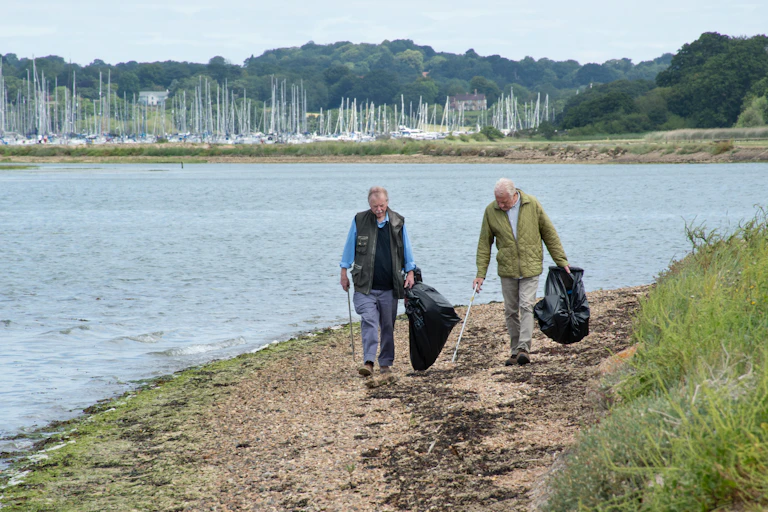 Two elderly men collecting litter on the shore.