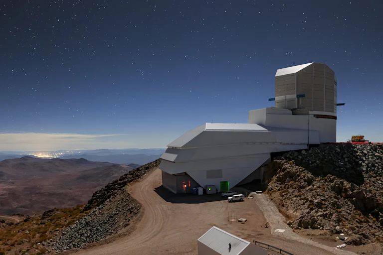 A telescope facility, which is a building with a curved dome on top, sitting on a mountain.