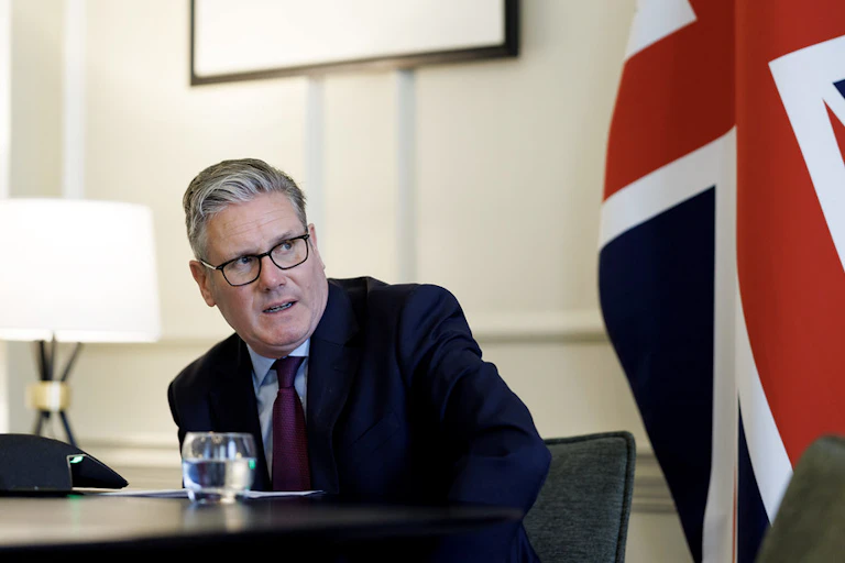 Keir Starmer leaning over his desk to speak on a phone call, with a UK flag behind him