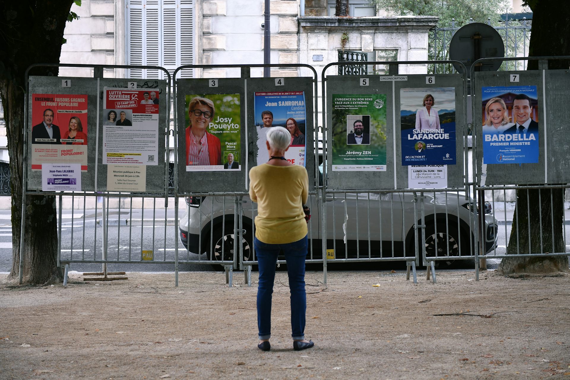 Une personne regarde plusieurs affiches électorales les bras croisés lors de la campagne précédant le second tour des élections législatives de 2024.