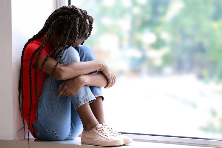 A sad girl sitting next to a window