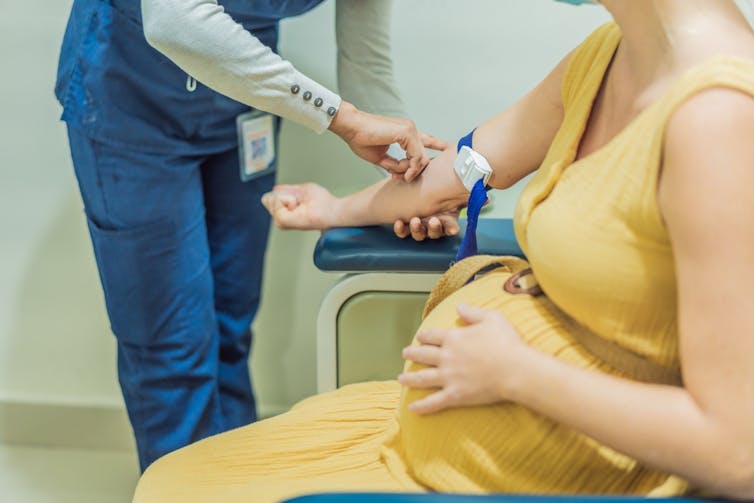Pregnant woman sitting in chair while health worker takes blood sample from right arm