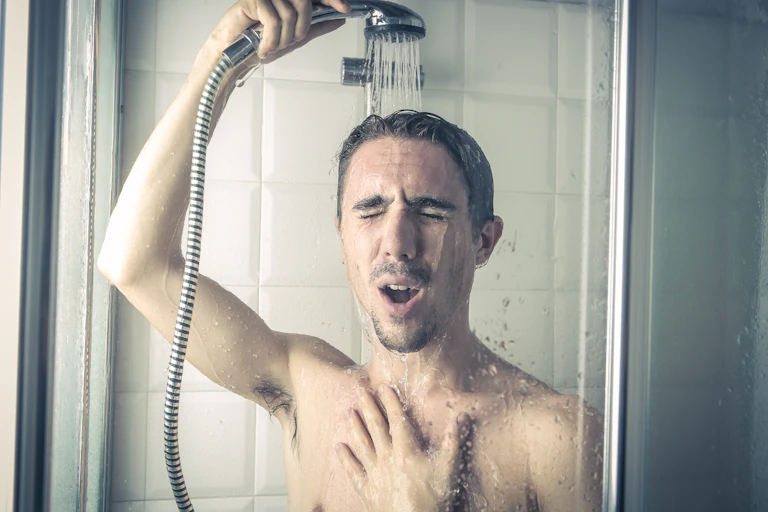 A man takes a cold shower. He's holding the shower head over his hair.