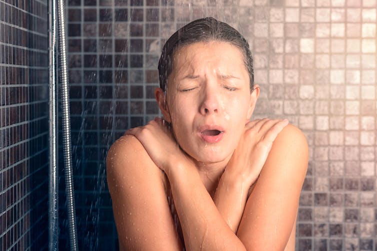 A woman shivers from the cold while taking a shower.