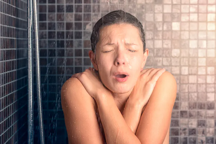 A woman shivers from the cold while taking a shower.