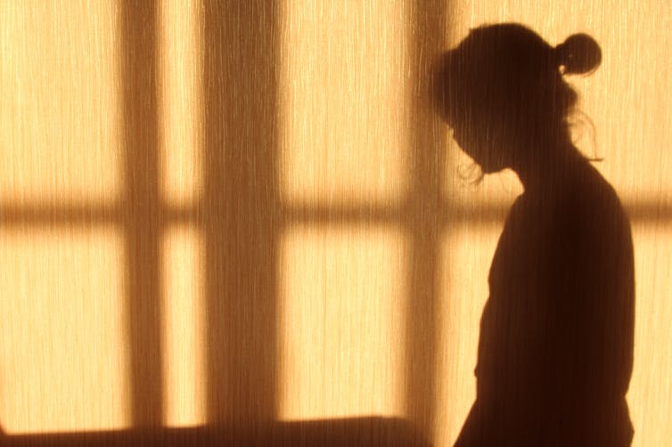 Silhouette of a young woman against a yellow wall