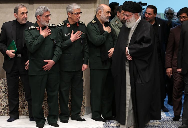 A man in traditional Iranian dress meat a group of men in army fatigues.