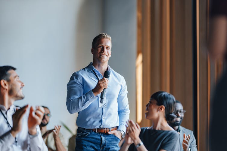 A man speaks while holding a microphone.