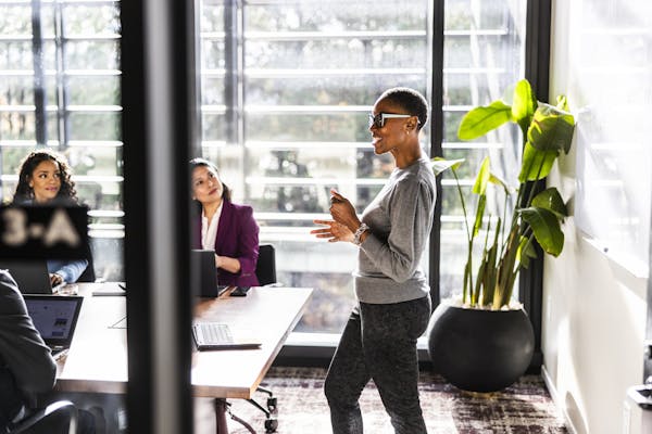 A woman wearing glasses speaks to people in a sun-filled conference room