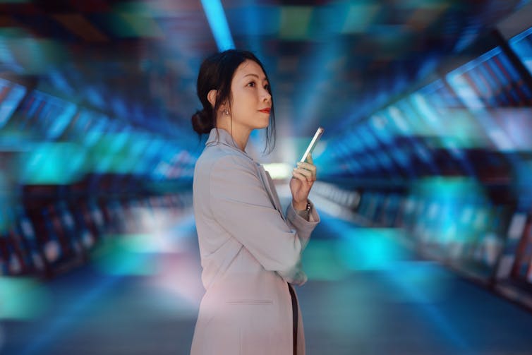 A businesswoman holding a smartphone stands in front of a computer generated background