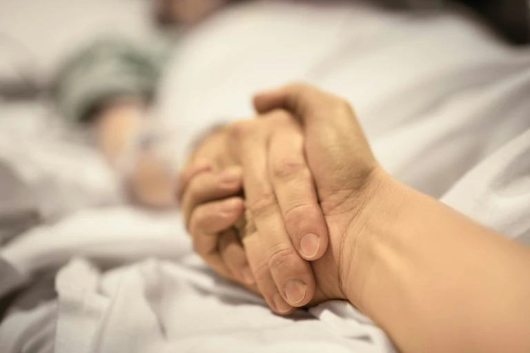 Two hands held on a bed
