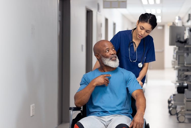 professionnelle de la santé avec un patient en chaise roulante dans un corridor d’hôpital