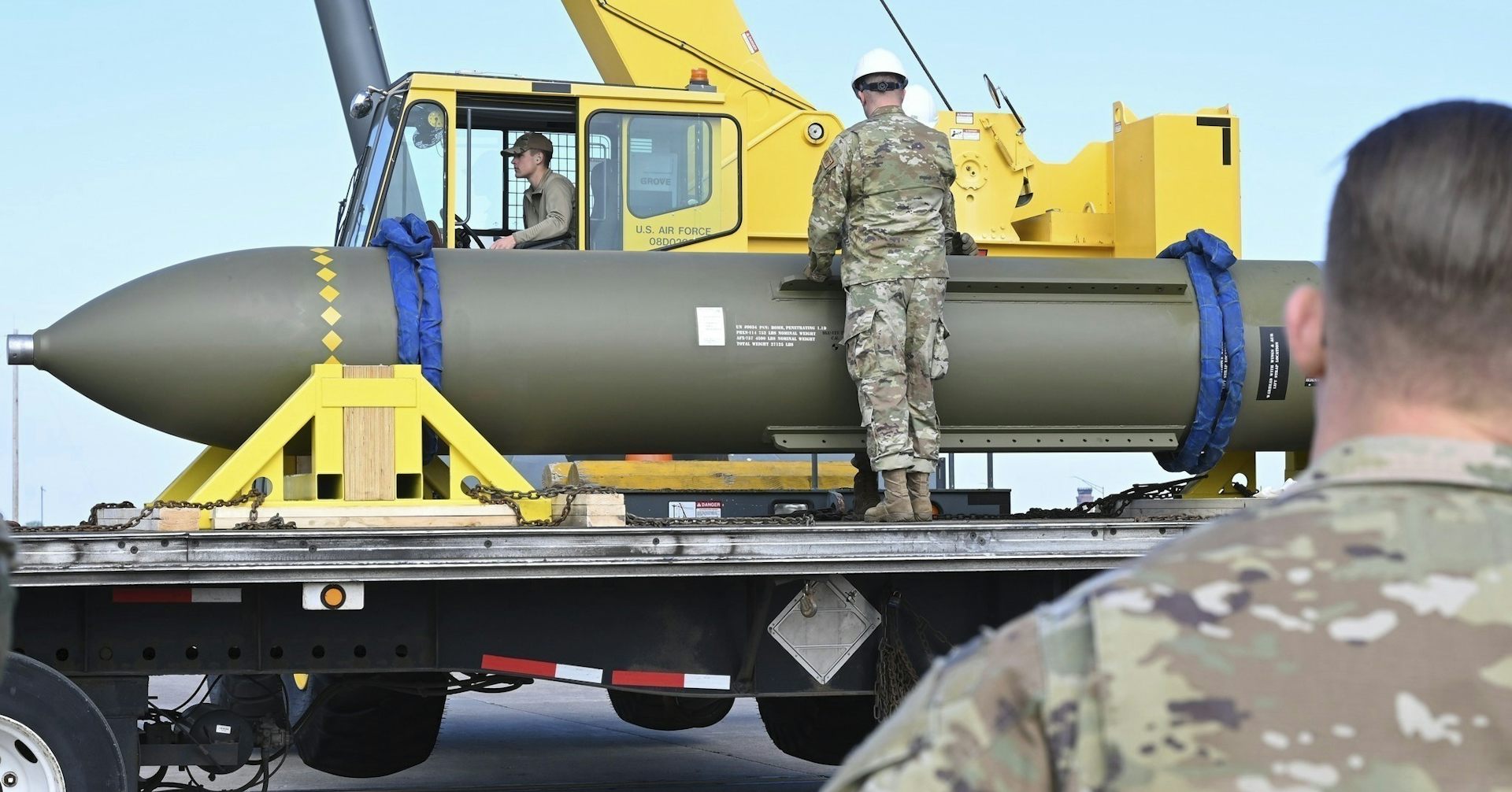 Photo of men in uniform looking at a huge bomb on the back of a truck.