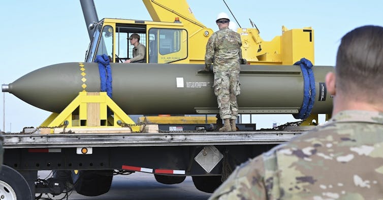 Photo of men in uniform looking at a huge bomb on the back of a truck.