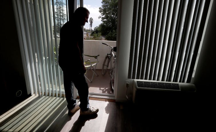 Silhouette of older man standing at sliding glass door.