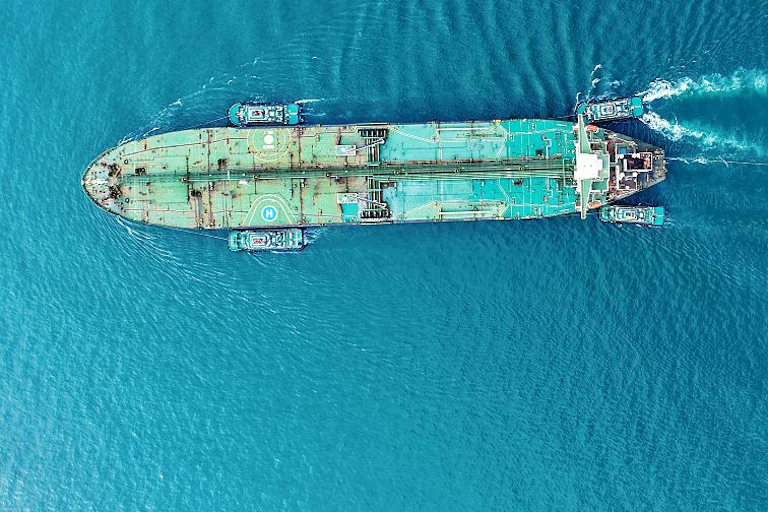 A cargo ship travelling through blue waters with smaller boats surrounding it.