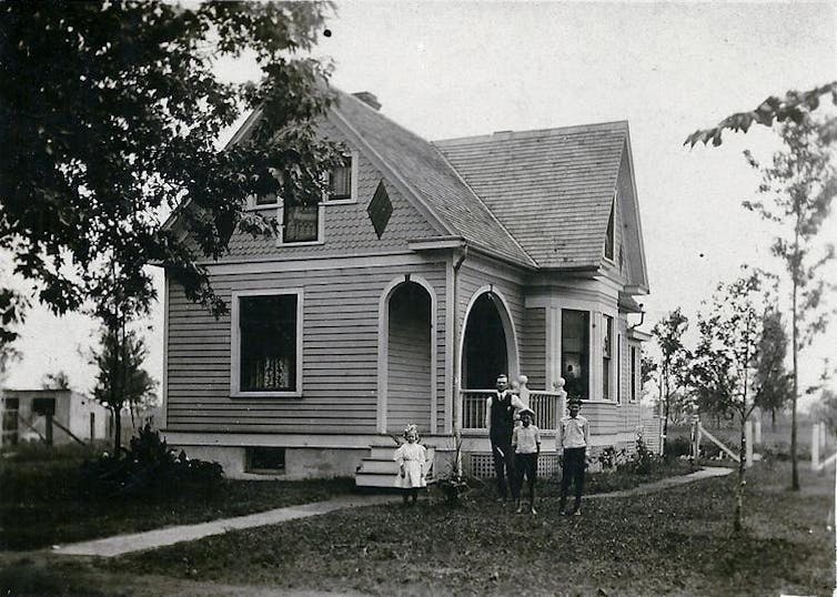 Black and white photo of family standing in front of their home.