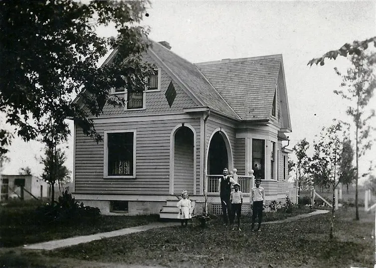 Black and white photo of family standing in front of their home.